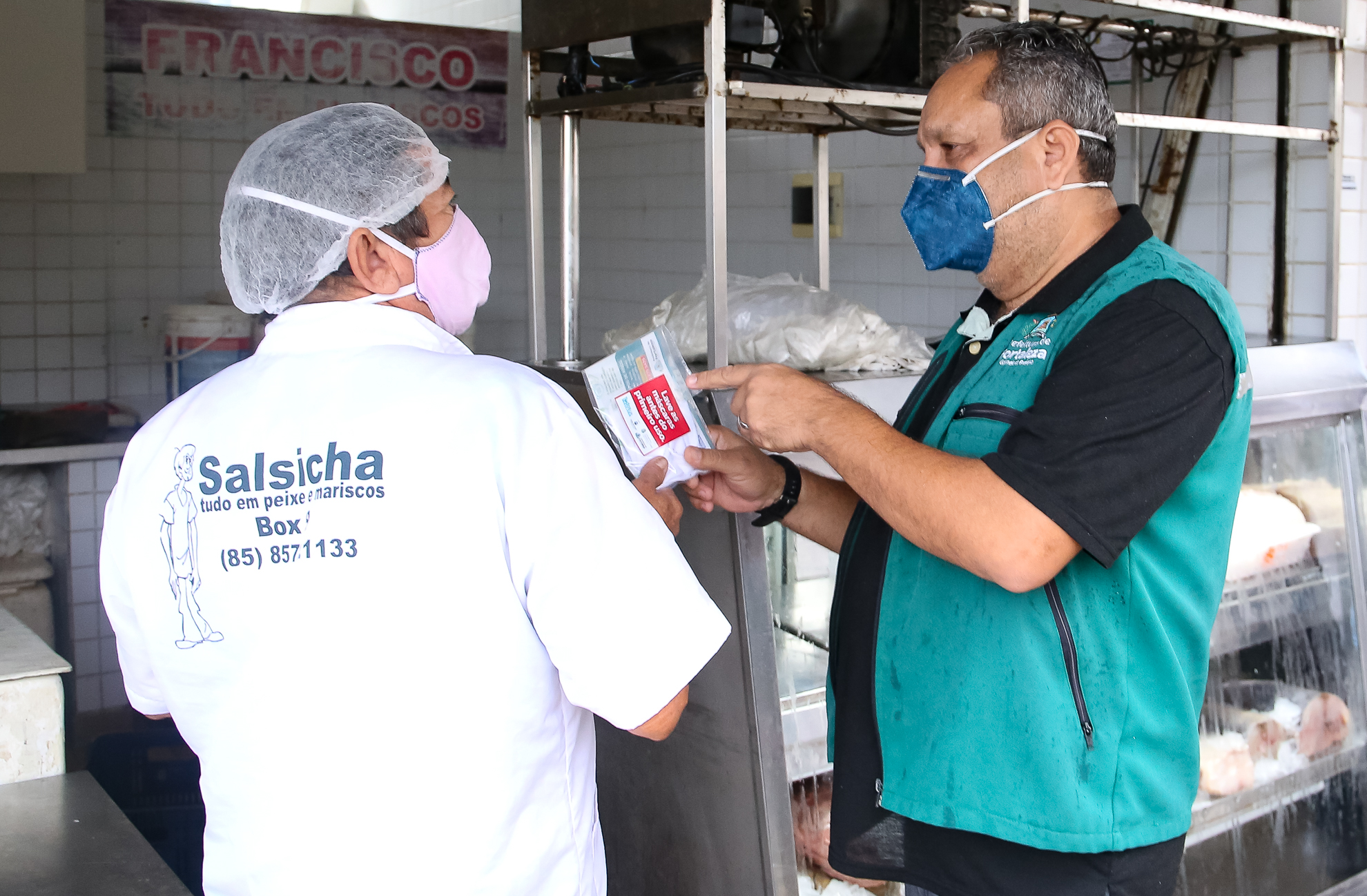 funcionário da prefeitura entrega um pacote com máscara protetora a um vendedor no mercado dos peixes